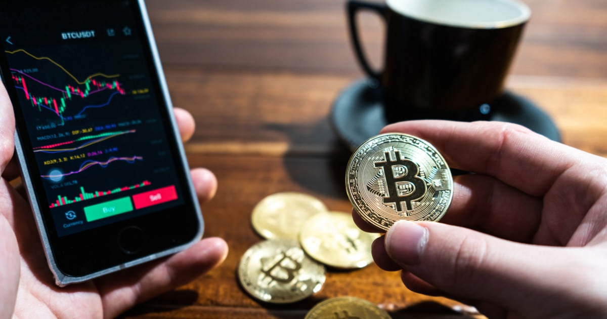 holding a bitcoin and using smartphone to trading the coin
