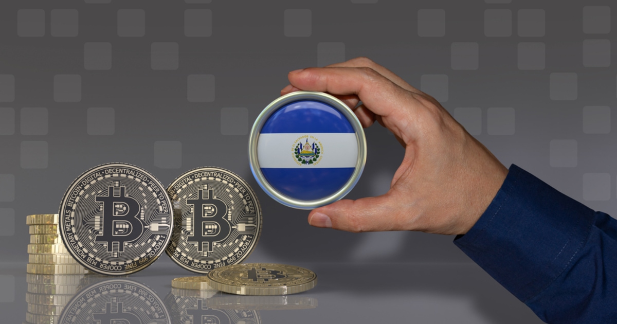 A hand holding aEl Salvador's flag coin and bitcoin on the desk